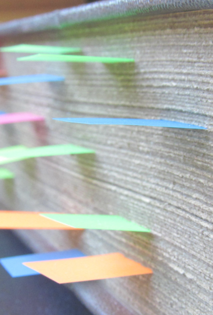 The picture shows a thick book where you can see a lot of colorful post-its sticking out.